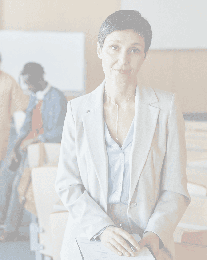 A senior leader in a light grey suit stands in a lecture theatre, students talking together behind her