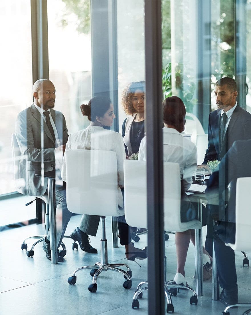 Business professionals gathered around a table in a glass-walled meeting room